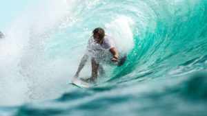 A man bent down, surfing a big blue wave.