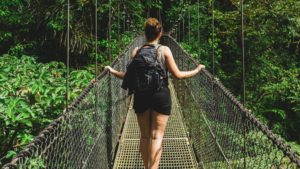 A women with a rucksack walking along a bridge in the rainforest.