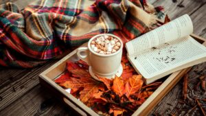 Hot chocolate with marshmallows in a tray full of leaves next to a blanket.
